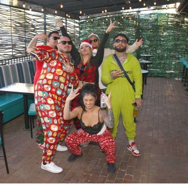 Six people in festive pajamas pose for a group photo on an outdoor patio.