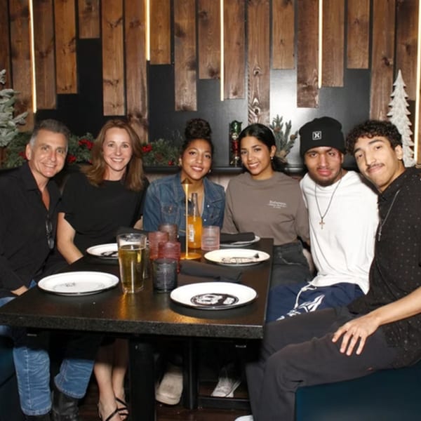Six people, three men and three women, smiling at a table in a dimly lit restaurant.