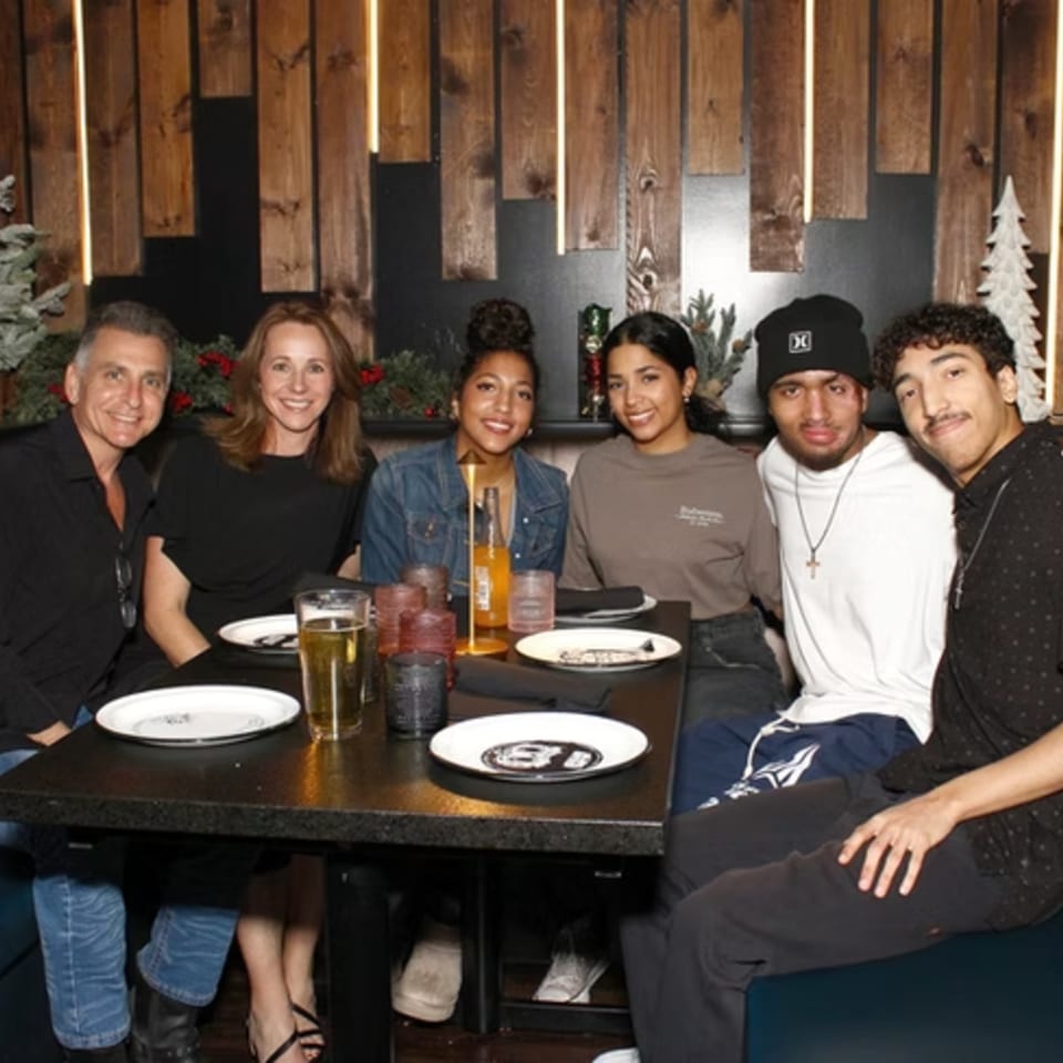 Six people, three men and three women, smiling at a table in a dimly lit restaurant.