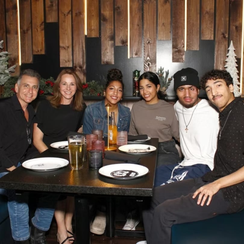 Six people, three men and three women, smiling at a table in a dimly lit restaurant.