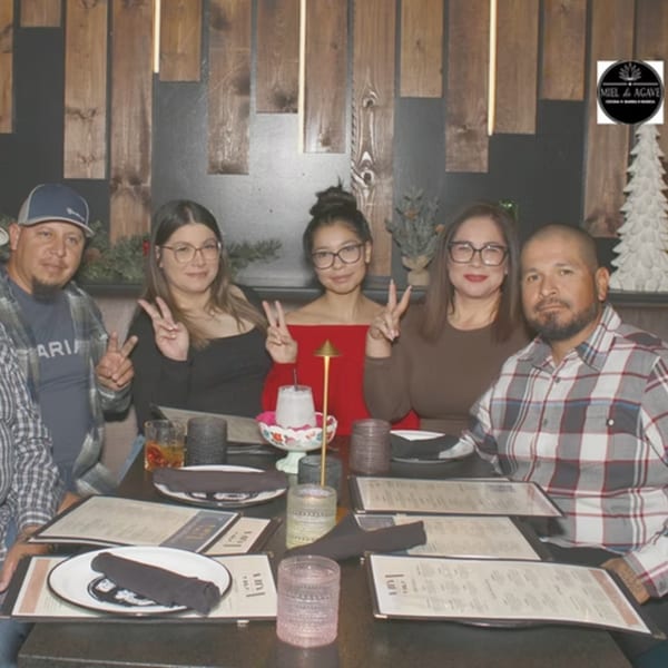 Five people, three women and two men, pose with peace signs at a restaurant table.