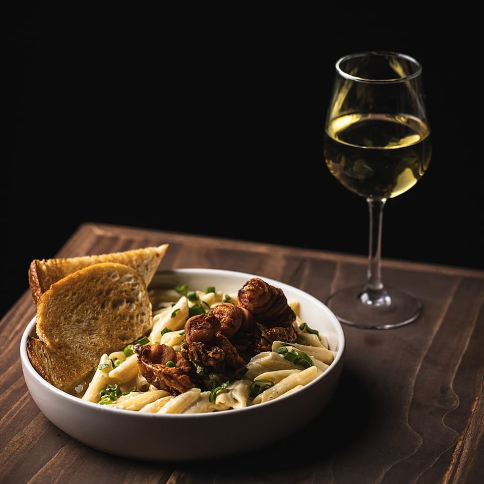 Creamy pasta with fried mushrooms, toasted bread, and a glass of white wine on a wooden table.