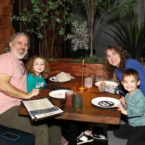 A family of four, two adults and two children, smiling at a restaurant table.