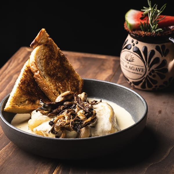 Creamy dish with roasted mushrooms and toasted bread, next to a decorative ceramic mug with a drink.