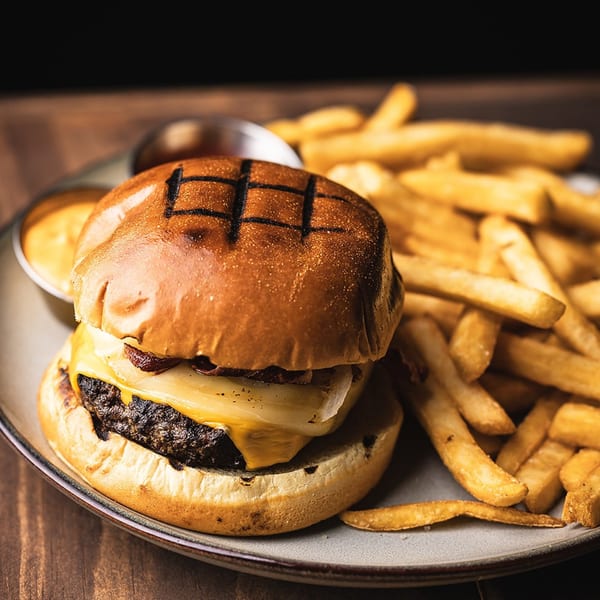 Cheeseburger with grilled onions and a side of golden fries and dipping sauce on a plate.