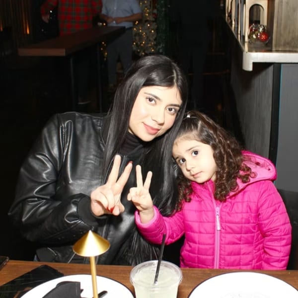 A woman and a young girl in a restaurant, both making peace signs at the camera.