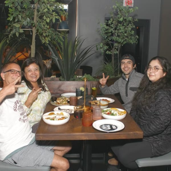 Four smiling people pose with peace signs around a table laden with food and drinks.