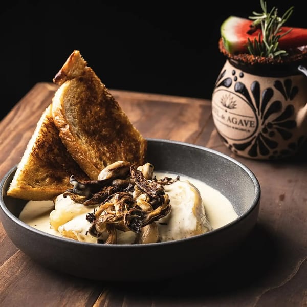 Savory dish with creamy sauce, roasted mushrooms, and toasted bread, next to a garnished cocktail.